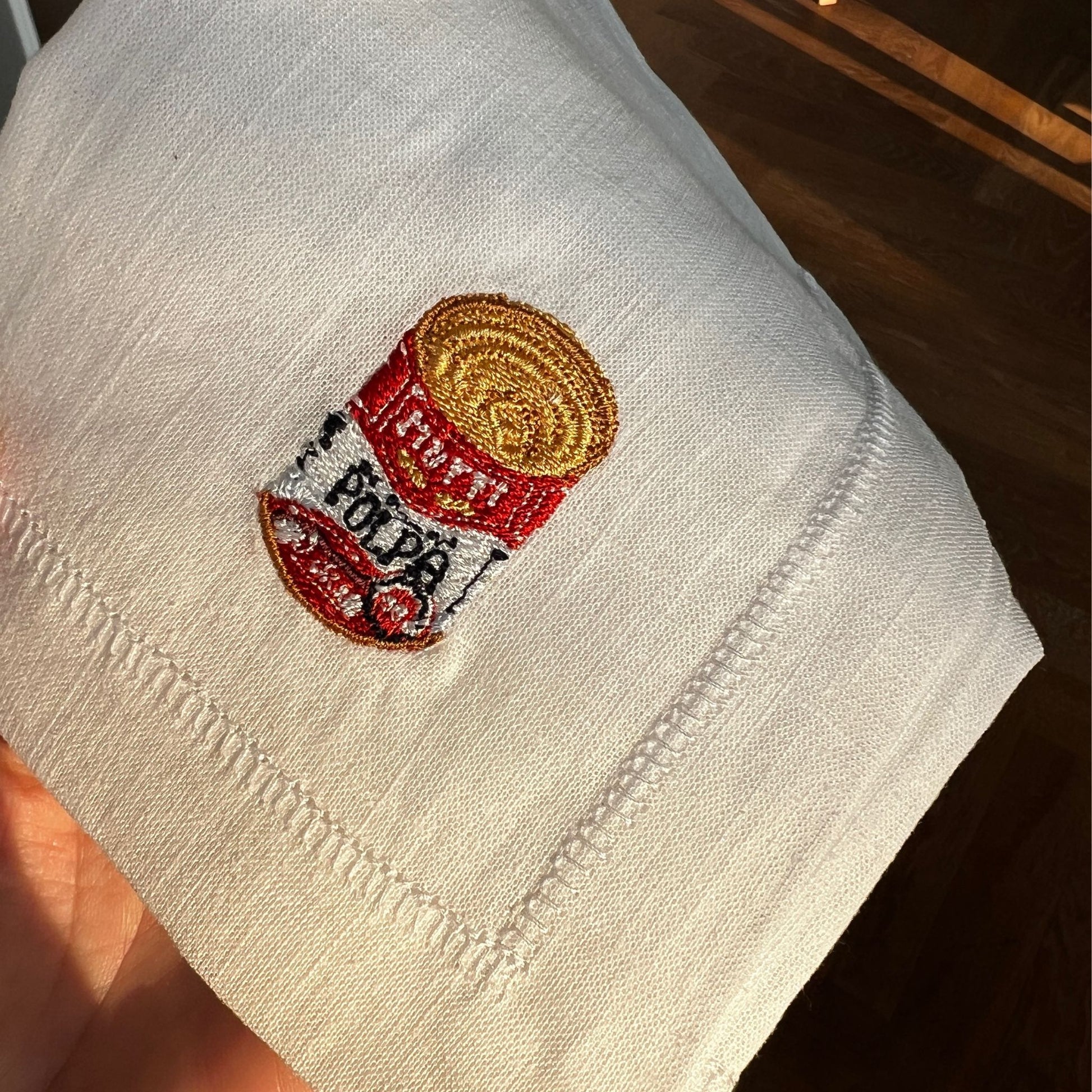 Detailed embroidery of illustration by Stefanie Viëtor of Polpa Mutti Can on white linen napkin with hemstich of 40x40cm