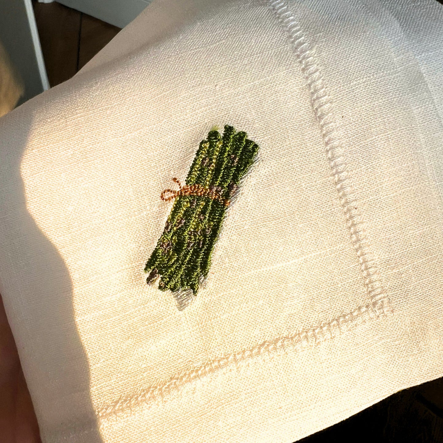 Detailed embroidery of illustration by Stefanie Viëtor of asparagus on white linen napkin with hemstich of 40x40cm