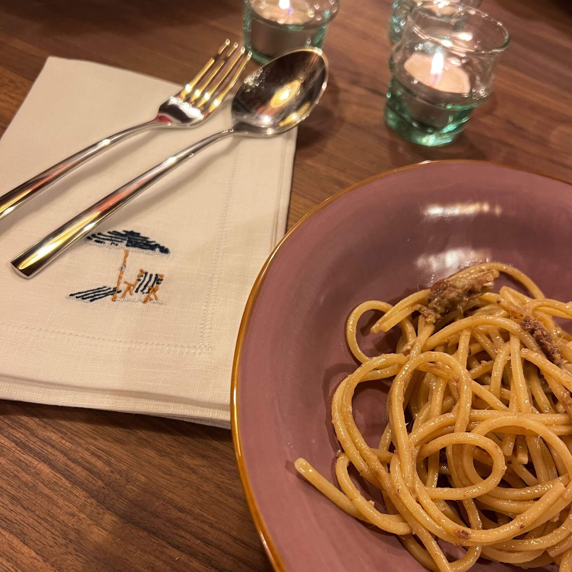 White linen napkin size 40x40cm embroidered illustration by Stefanie Vietor of beach scene with blue ombrellone in dinner table setting