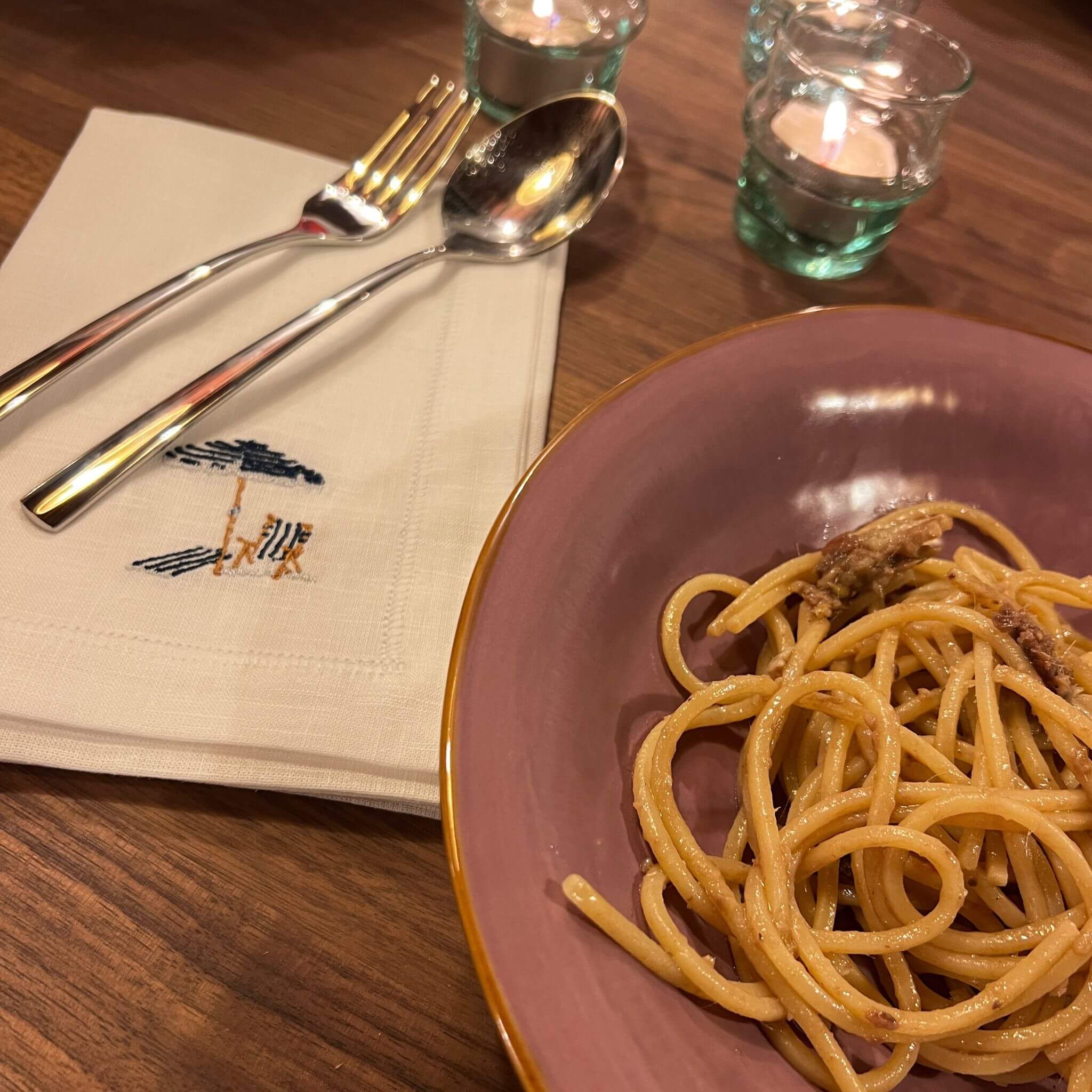 White linen napkin size 40x40cm embroidered illustration by Stefanie Vietor of beach scene with blue ombrellone in dinner table setting